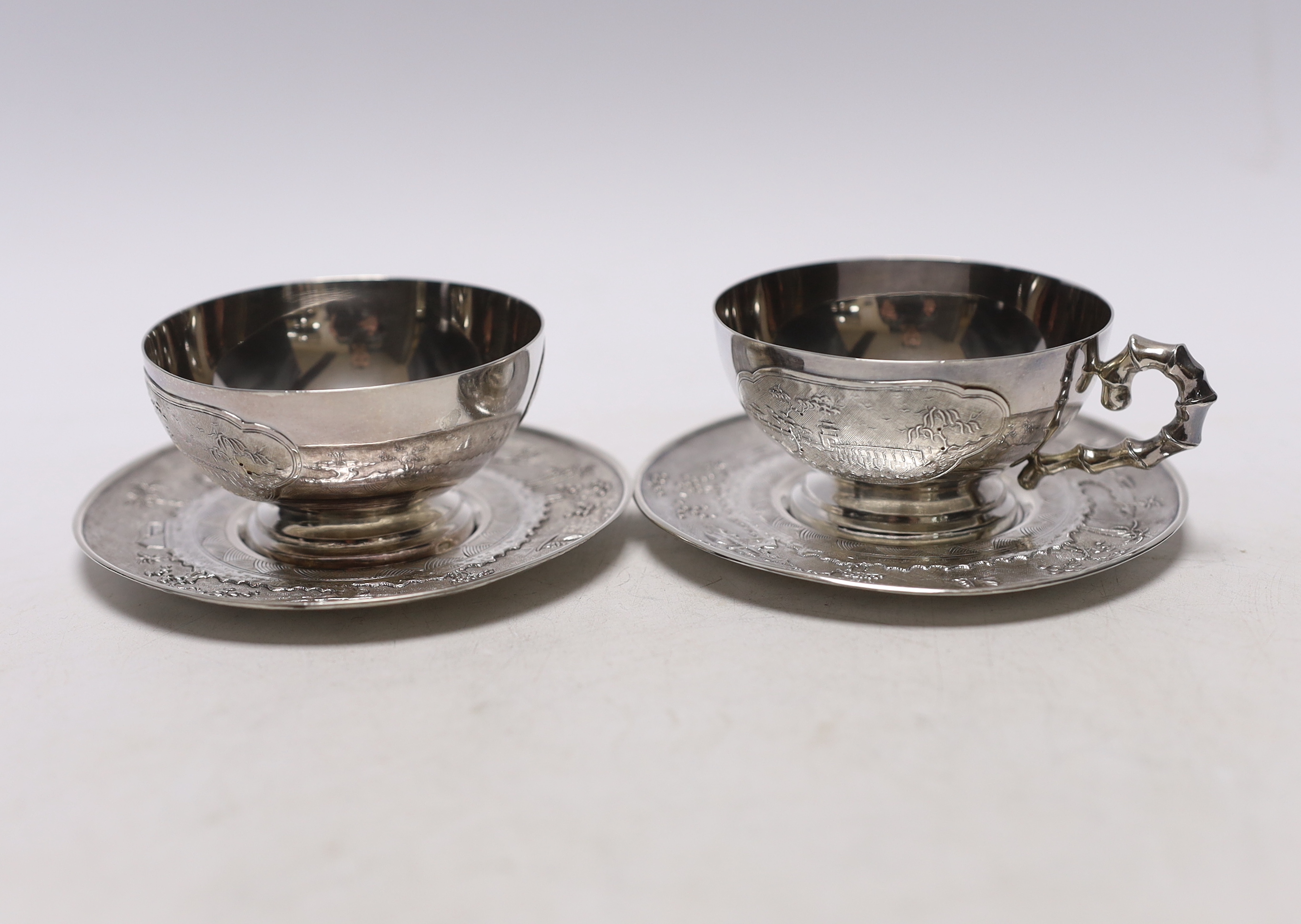 Two early 20th century Vietnamese 800 standard white metal tea cups and saucers (one lacking handle), saucer diameter 10.1cm, 6.6oz.